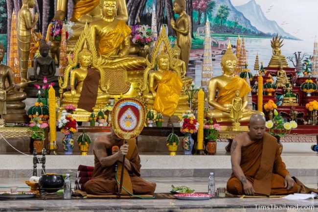 monk giving sermon while sitting in front of Buddha images