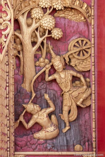 woodcarving of man lifting a chariot over his head.