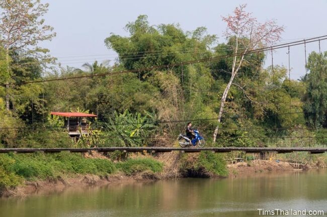 motorcycle riding over a river on a suspension bridge