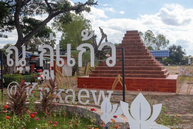 Ku Kaew sign in park with laterite pyramid behind it