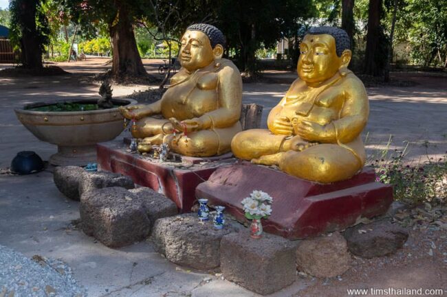 two Phra Sangkajai statues with laterite blocks around them