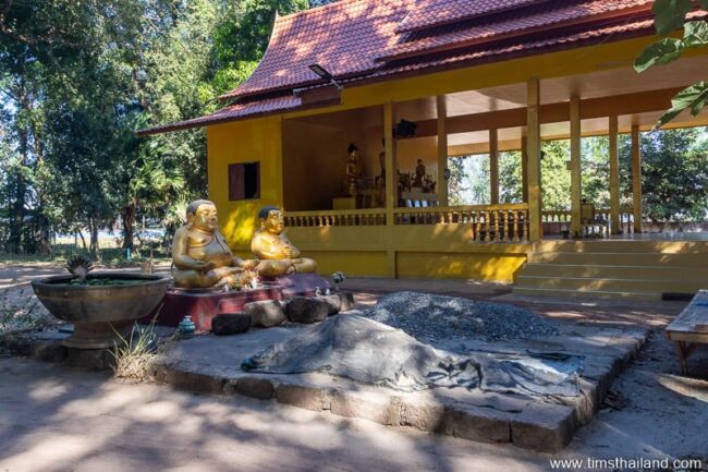 two Phra Sangkajai statues with laterite blocks around them