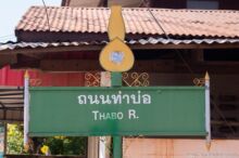 <b>Tha Khantho, Kalasin province</b><br>This district was named after an old type of jug, called a <i>khantho</i> in Thai, because the land lays between two rivers and once had that shape. green street sign with a yellow jug on top